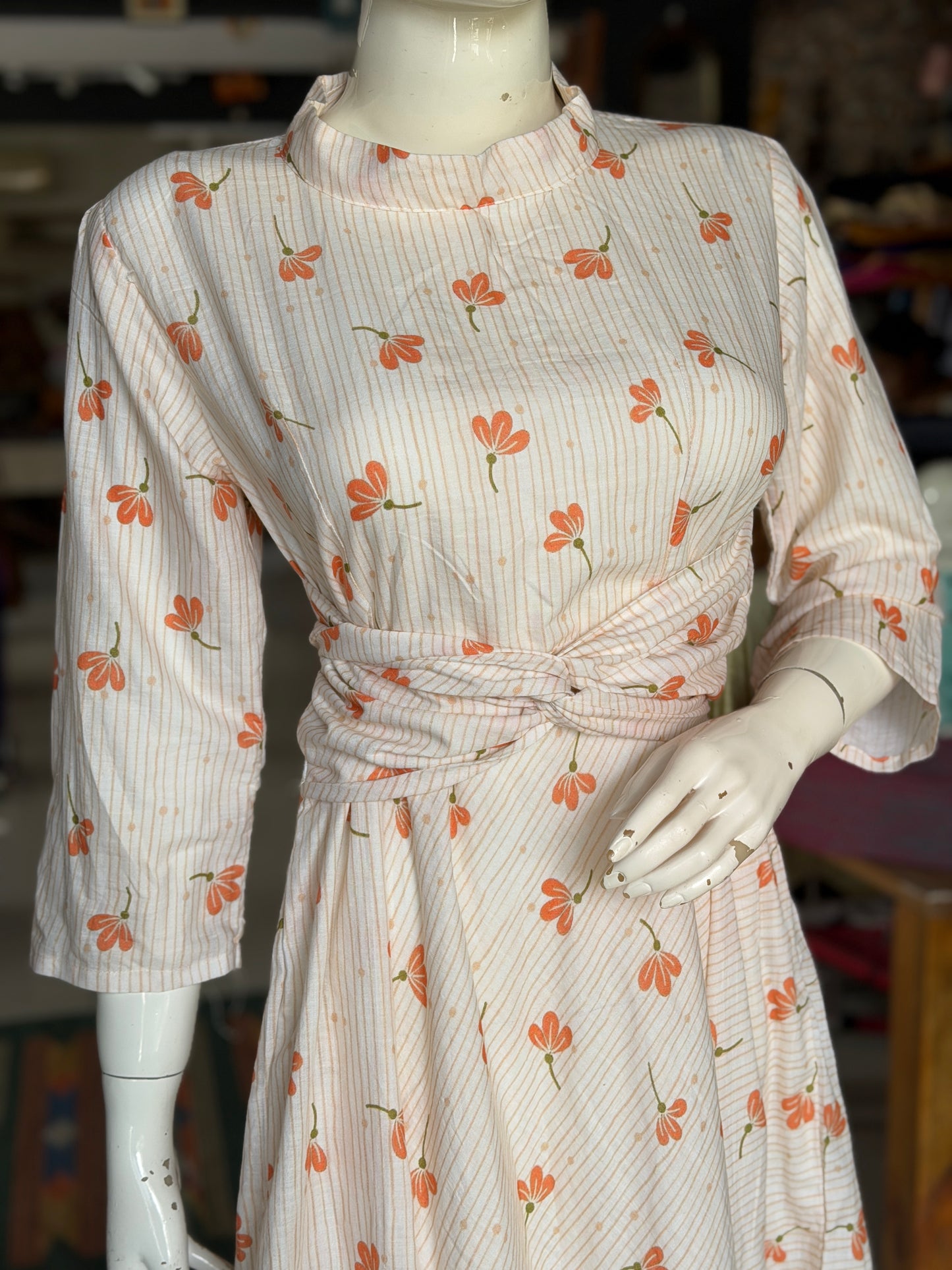 Peach floral print on off white soft cotton umbrella dress with band collared neck, long sleeves and waist belt