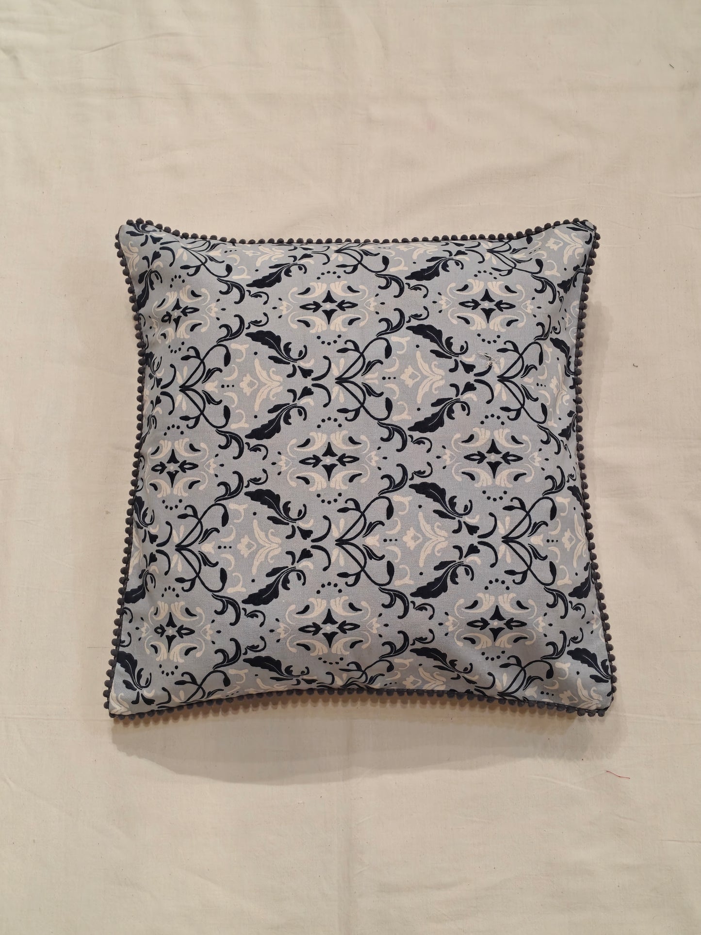 Cushion cover with blue and white patterns and pom pom borders