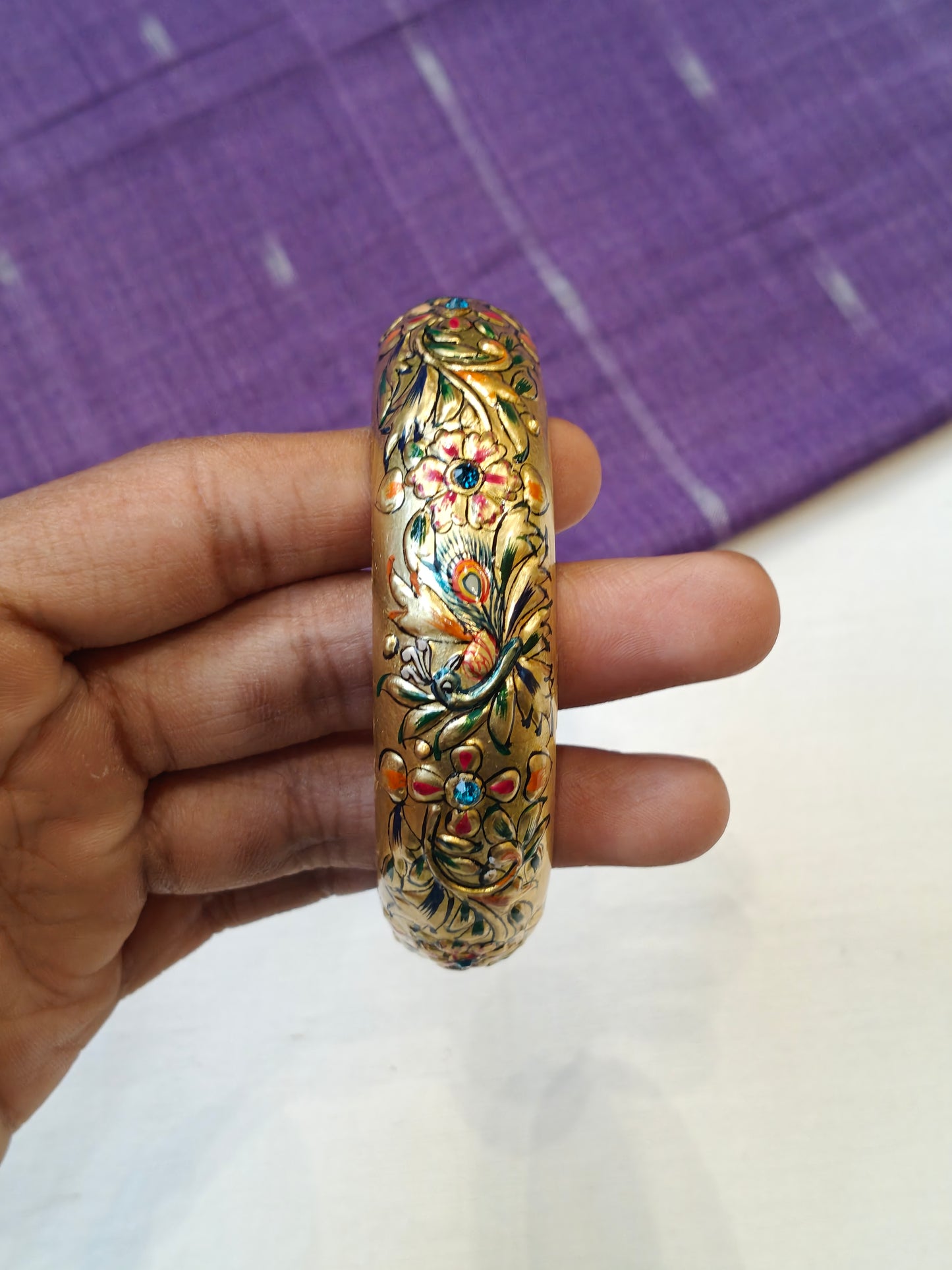 Single gold embossed wide bangle with peacock design and blue stones